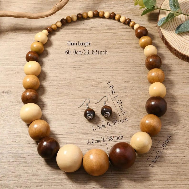 May include: A wooden bead necklace and matching earrings set. The necklace features various sizes of round wooden beads in shades of brown and cream. The chain length is 23.62 inches. The earrings are dark brown with a silver-colored floral design.