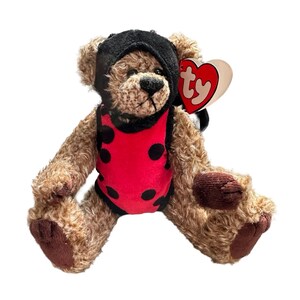 May include: A brown plush teddy bear wearing a black hood and a red leotard with black polka dots. The bear has dark brown paw pads and a heart-shaped tag attached to its ear with the letters ty printed in red on a cream background.
