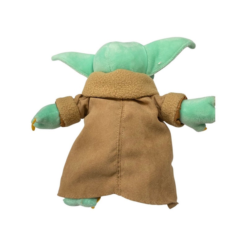 May include: A plush toy of a character from a popular science fiction series. The toy has large, pointed ears, green skin, and is wearing a tan coat with a brown collar. The toy's arms are outstretched.