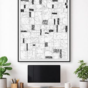 May include: Black framed abstract art print with a geometric design. The artwork features a grid of textured squares with black brushstroke-like shapes. The print hangs above a wooden desk with a computer, plants, and office supplies.