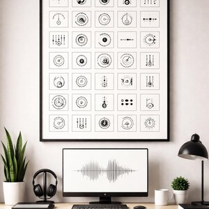 May include: A framed print featuring a grid of black and white abstract designs hangs above a desk. The desk holds a computer monitor displaying a sound wave, headphones, a keyboard, and a small potted plant. A black desk lamp and a mug are also visible.