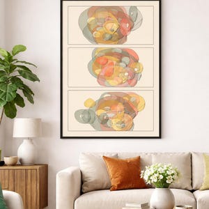 May include: Abstract art print in a black frame. The artwork features three horizontal panels, each displaying a colorful, overlapping circular design in shades of orange, yellow, and gray. The print hangs above a beige sofa with an orange pillow.