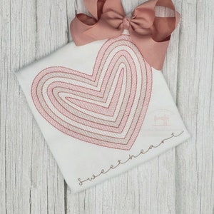 May include: A white t-shirt with a pink and red embroidered heart design and the text "sweetheart" in pink embroidery.