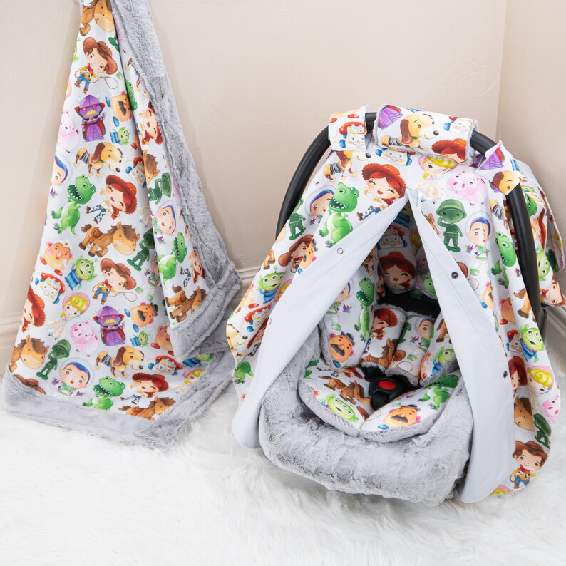 May include: A gray and white car seat cover with a Toy Story theme. The cover features a variety of Toy Story characters, including Woody, Buzz Lightyear, and Jessie. The cover is made of soft, comfortable fabric and is perfect for protecting your car seat from spills and stains.