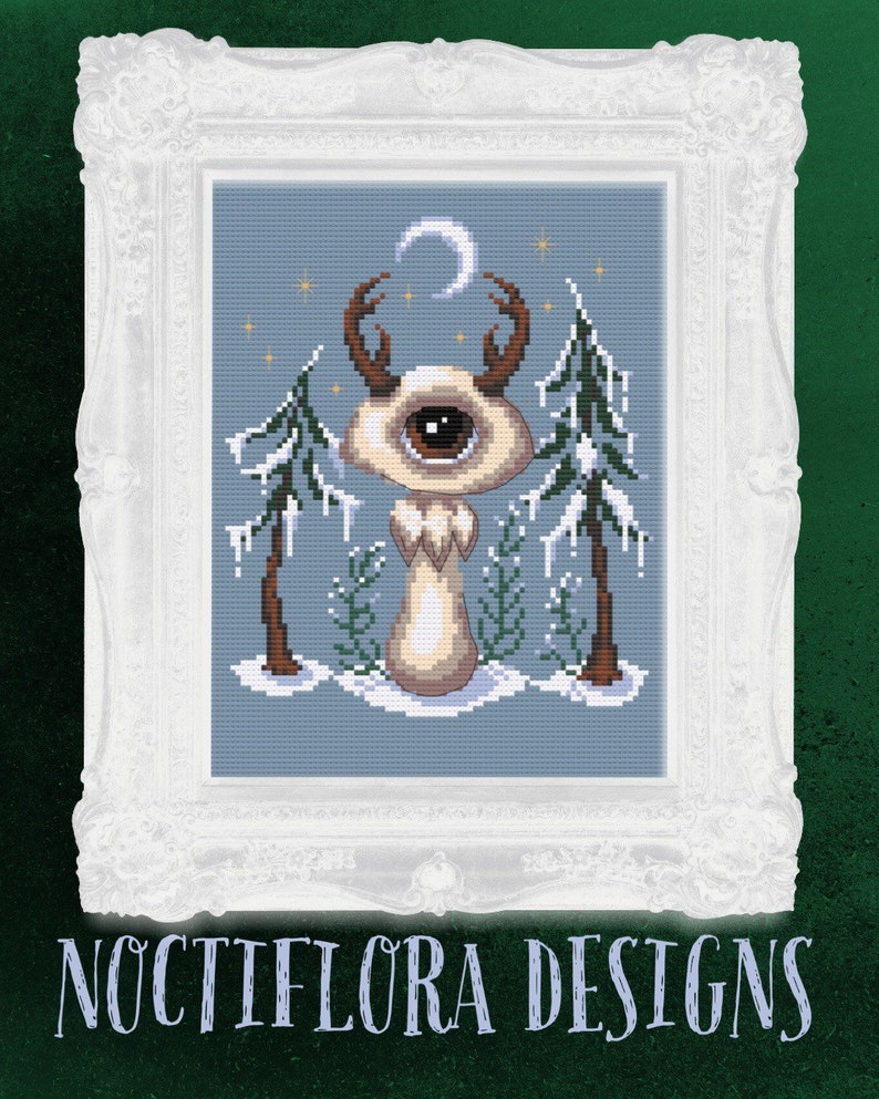 May include: A cross-stitch pattern featuring a whimsical creature with a single eye, antlers, and a crescent moon above its head. The creature is standing in a snowy forest with pine trees and icicles. The pattern is framed in a white ornate frame.
