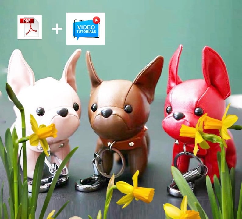 May include: Three plush French bulldog keychains, one pink, one brown, and one red, with spring-loaded rings. Each keychain is holding a yellow daffodil flower.