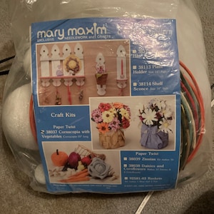May include: A craft kit by Mary Maxim, featuring paper twist and needlework projects. The kit includes materials for making a cornucopia with vegetables (10" long), plant holders (14" high), and shelf sconces (14" high). Also included are materials for making zinnias and daisies.
