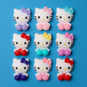 May include: Nine white cat-shaped figurines with different coloured bows and bottoms, including purple, pink, blue, red, and yellow. The figurines have black eyes and whiskers, set against a solid blue background.