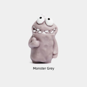 May include: A gray monster figurine with a big smile and white teeth. The monster has two large eyes and a small bump on its head. The figurine is made of a soft, pliable material.