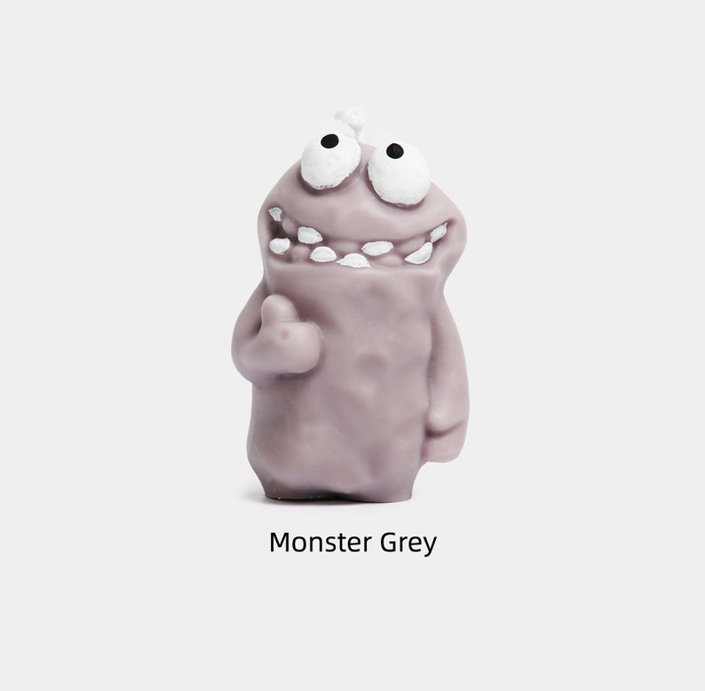 May include: A gray monster figurine with a big smile and white teeth. The monster has two large eyes and a small bump on its head. The figurine is made of a soft, pliable material.