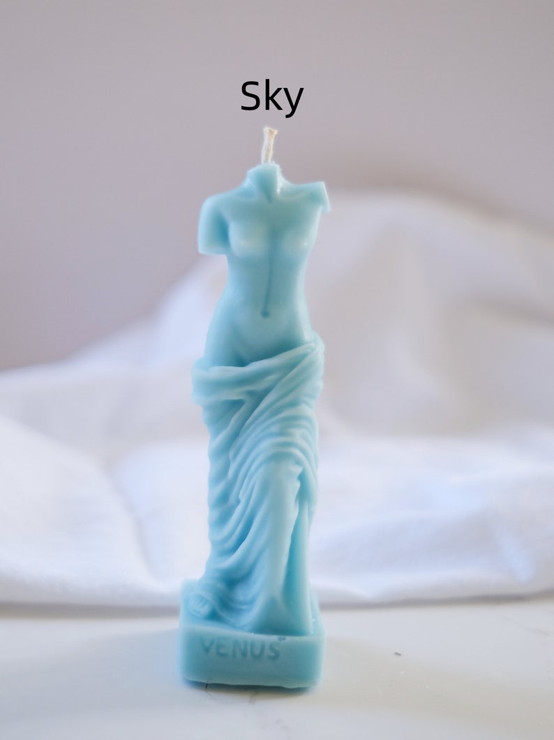 Op de afbeelding: Een lichtblauwe kaars in de vorm van het standbeeld van de Venus van Milo. De kaars heeft een witte lont en de basis van de kaars heeft de tekst "VENUS".