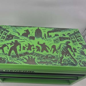May include: A green metal tool chest with a zombie-themed graphic on the lid. The graphic features zombie figures, buildings, and the text "U.S. GENERAL". The chest has multiple drawers.