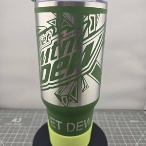 以下が含まれることがあります： シルバーのDiet Mtn Dewロゴが施された、グリーンのパウダーコーティング仕上げのステンレス製タンブラー。透明なプラスチック製の蓋、ライムグリーンのシリコン製ベースを備え、下部のグリーン部分には白い文字でDIET DEWとプリントされています。
