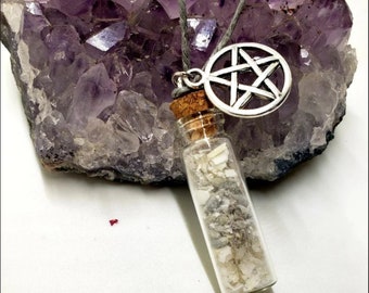 Könnte beinhalten: Ein silberner Pentagramm-Anhänger hängt an einer grauen Kordelkette mit einem kleinen Glasfläschchen, das mit weißen Kristallen gefüllt ist. Das Fläschchen hat einen Korkverschluss und hängt am Anhänger.