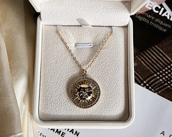 May include: A gold necklace with a sun pendant in a white box. The box has the text 'Entry $30 +000 000 0000 Santa, C.A.901912' printed on it.