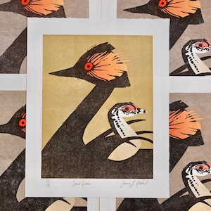 Op de afbeelding: Kunstafdrukken met een gestileerde illustratie van een vogel met een lange nek en oranje accenten. De prints hebben een minimalistisch ontwerp met een neutraal kleurenpalet en zijn gesigneerd door de kunstenaar.