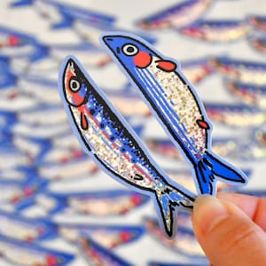 May include: Two blue and silver glitter fish stickers with red and white details. The fish are facing opposite directions and are arranged in a V-shape.