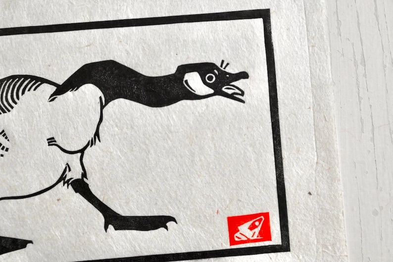 May include: Black and white illustration of a goose with its head turned to the right. The goose is running. A red and white illustration of a frog is in the lower right corner.