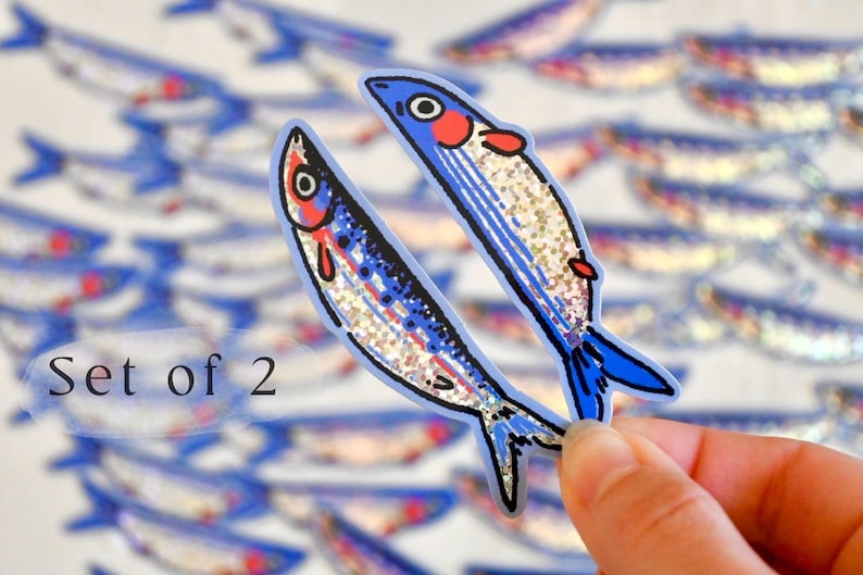 May include: Set of two blue and silver glitter fish stickers. The fish have red and white details on their faces. The stickers are perfect for adding a touch of whimsy to your crafts, journals, or laptops.
