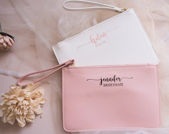 May include: Two personalized clutches, one white with "helen bride" written on it and one pink with "jennifer bridesmaid" written on it.