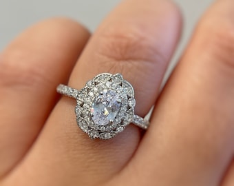 May include: A silver ring with an oval-shaped center stone surrounded by a double halo of smaller stones.