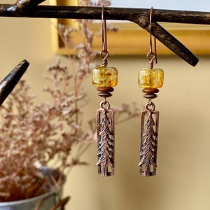 May include: Copper earrings with a tree design and amber glass beads.