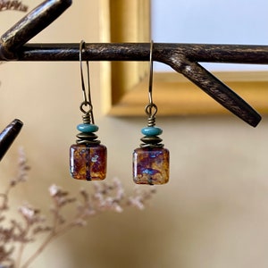May include: A pair of dangle earrings with a rectangular, iridescent, amber-colored glass bead, a turquoise bead, and a brass spacer bead on each earring.