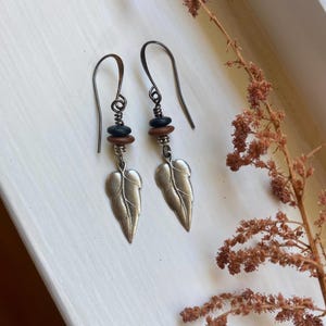May include: A pair of silver leaf earrings with brown and black beads. The earrings are hanging from silver hooks.