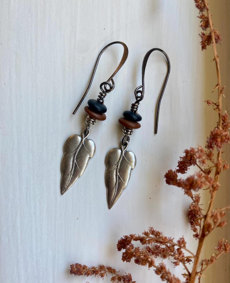 May include: Silver leaf earrings with brown and black beads hanging from a silver hook.