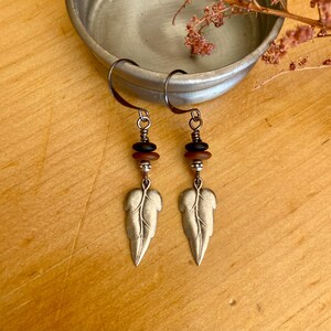 May include: Silver leaf earrings with brown and black beads. The earrings are hanging from silver hooks.