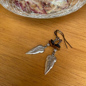 May include: Silver leaf earrings with brown and black beads hanging from silver hooks.