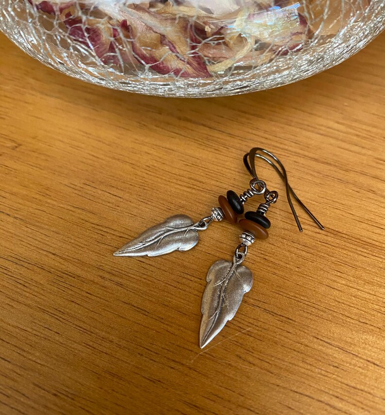 May include: Silver leaf earrings with brown and black beads hanging from silver hooks.