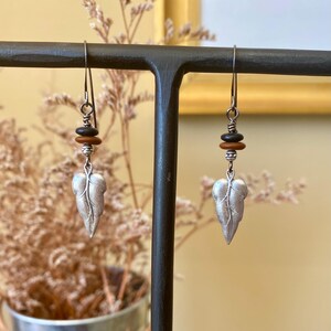 May include: Silver leaf earrings with brown and black beads hanging from a black metal stand.