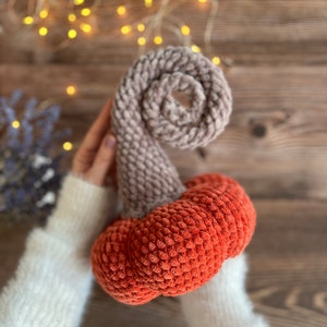 May include: A crocheted pumpkin with a brown stem and an orange body. The pumpkin is made with a fuzzy yarn.