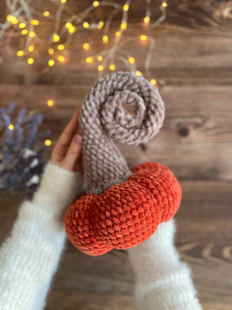 May include: A crocheted pumpkin with a brown stem and an orange body. The pumpkin is made with a fuzzy yarn.