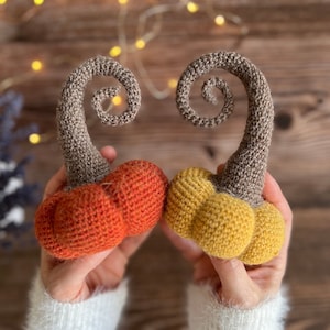 May include: Two crocheted pumpkins, one orange and one yellow, with brown stems that are curled into a spiral shape.