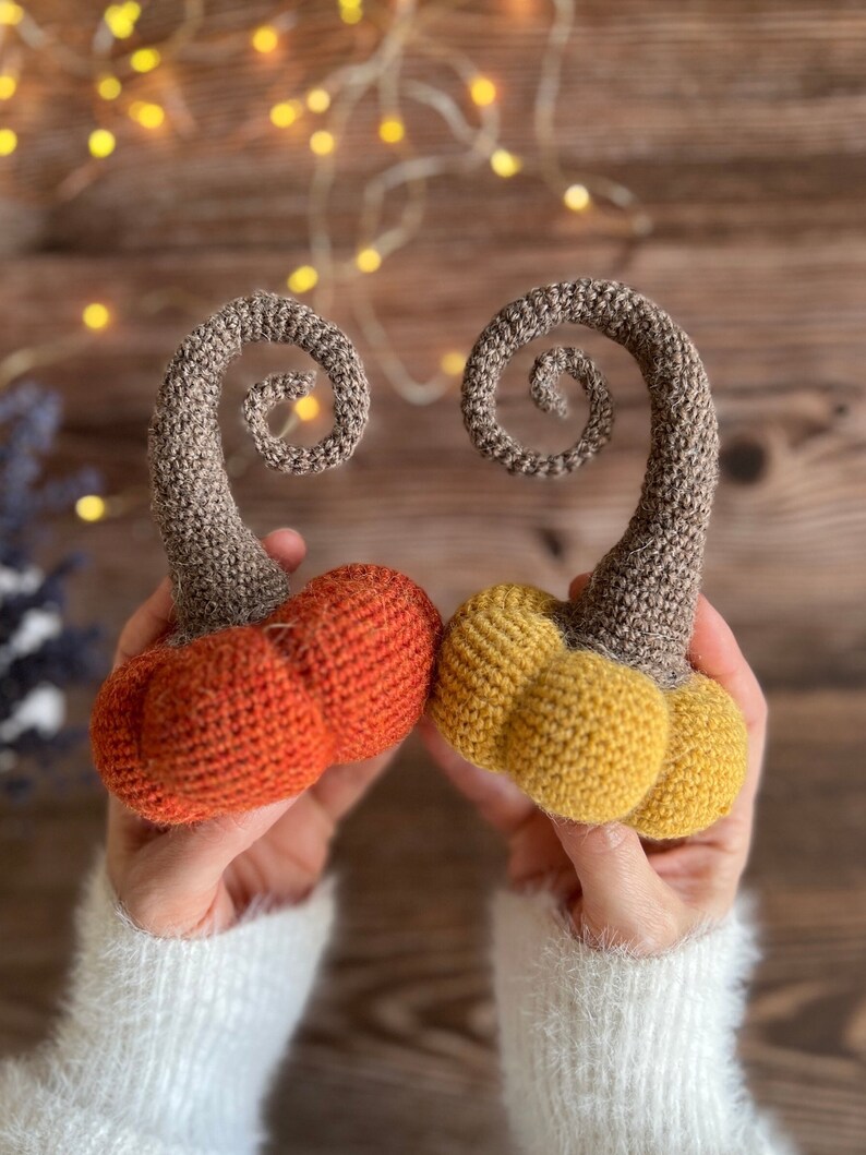 May include: Two crocheted pumpkins, one orange and one yellow, with brown stems that are curled into a spiral shape.