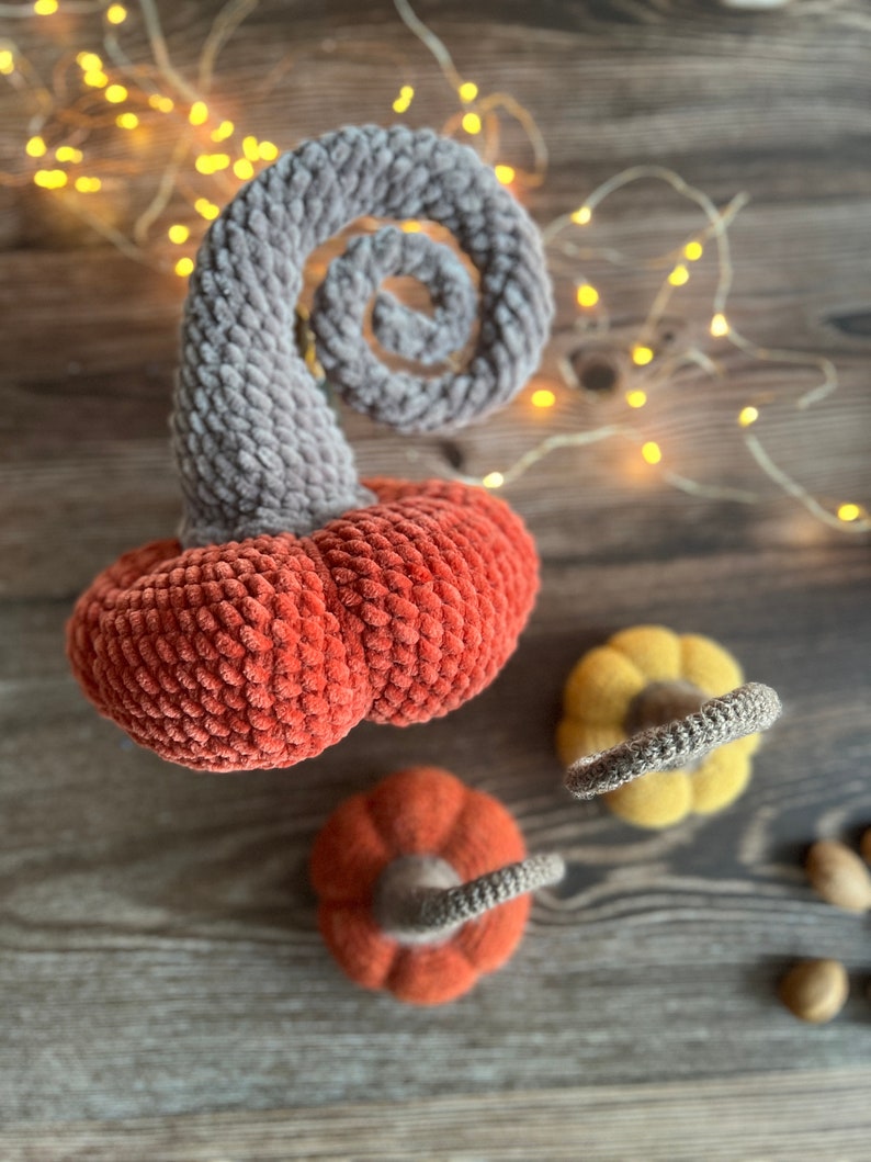 May include: Three crocheted pumpkins in orange, yellow, and gray. The pumpkins are made with a soft, fuzzy yarn and have a rustic, handmade look.