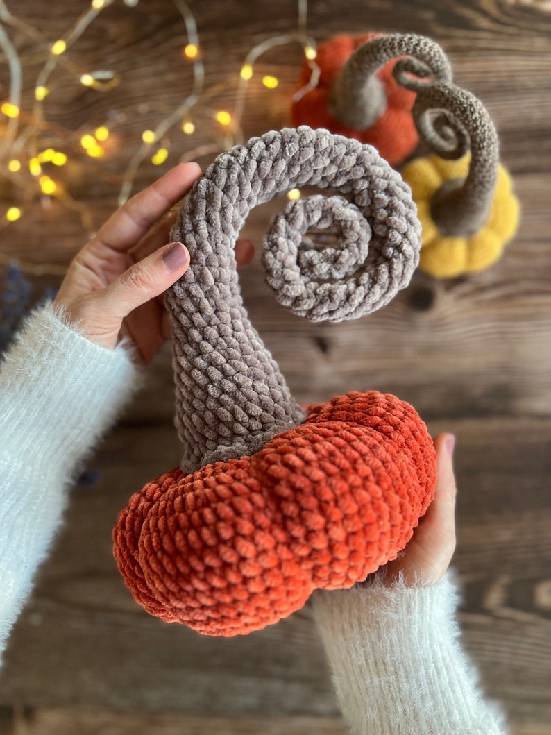 May include: Two crocheted pumpkins, one with a gray stem and a red body, and the other with a brown stem and a yellow body.