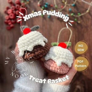 以下が含まれることがあります： 2つの編み物クリスマスプディングオーナメント。1つは茶色と白、もう1つはピンクと白です。それぞれに赤いさくらんぼと緑の葉が付いています。「xmas Pudding」と「Treat Basket」の文字が見えます。