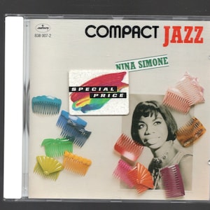 Può includere: Una custodia per CD con un'immagine colorata di Nina Simone. La custodia presenta il testo "Compact Jazz" e "Nina Simone" sul davanti. Il testo "Special Price" è su un adesivo nell'angolo in alto a sinistra dell'immagine. La custodia è circondata da una varietà di fermagli per capelli colorati.