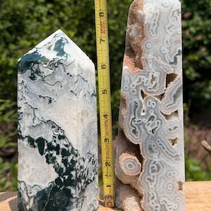 May include: Two polished stone towers with pointed tops. The left tower features dark green moss-like inclusions in white stone. The right tower displays intricate grey and white circular patterns with tan textured areas. A yellow ruler shows a height of 9 inches.