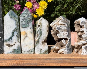 May include: Five polished moss agate crystal towers with white, green, and brown inclusions. The tallest tower stands approximately 12.7 cm high next to a black ruler. Each stone features unique natural patterns, crystalline cavities, and textures.
