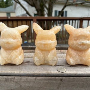 May include: Three small, hand-carved, yellow-orange, Pikachu figurines made of calcite.