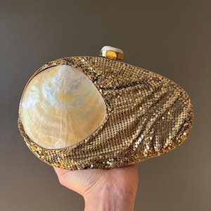 May include: Gold-toned mesh clutch with a large, pearlescent seashell accent. The clutch has a rounded shape and a small, decorative clasp. A unique evening bag.