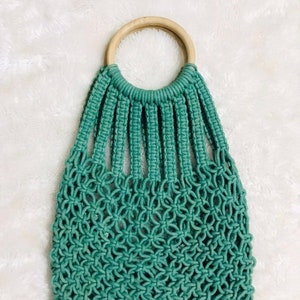 May include: A teal blue crocheted tote bag with a wooden ring handle. The bag is 28 by 32 centimeters.