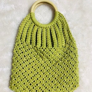 May include: A green crocheted tote bag with a wooden handle. The bag has a  mesh design and is perfect for carrying everyday essentials.