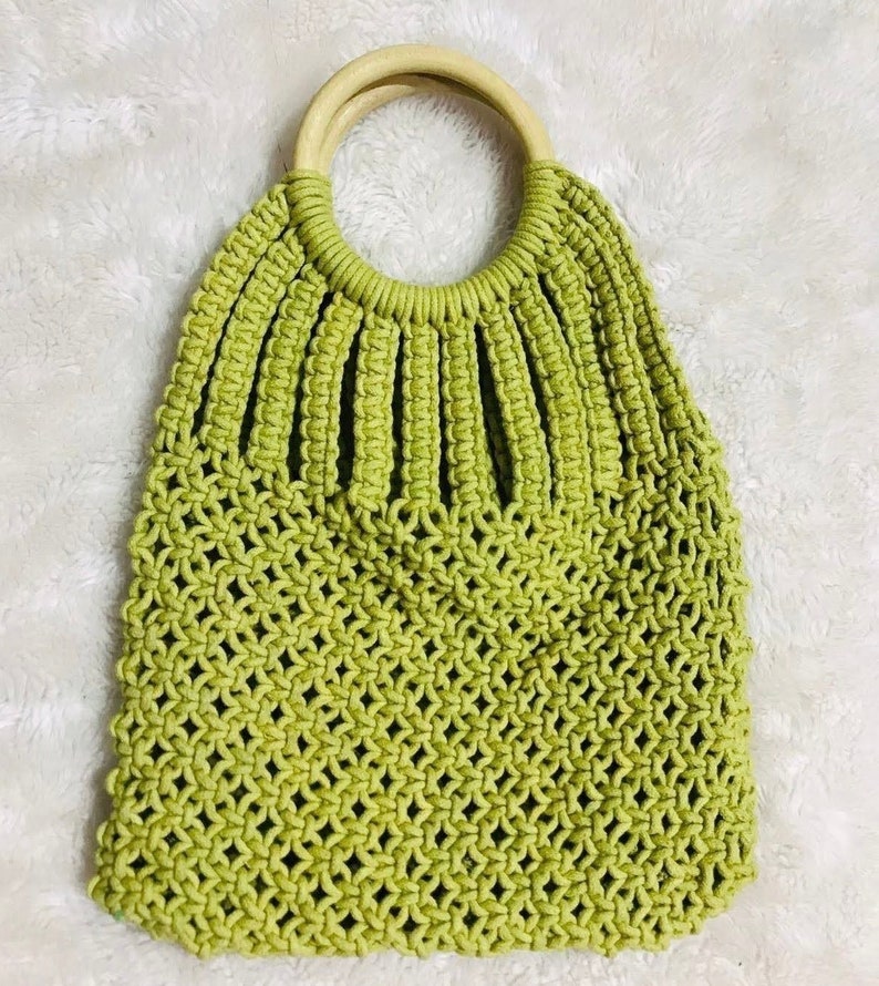 May include: A green crocheted tote bag with a wooden handle. The bag has a  mesh design and is perfect for carrying everyday essentials.