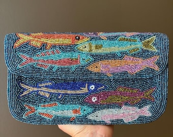 May include: A rectangular clutch bag covered in dark blue beads featuring a multi-colored beaded pattern of various fish. The fish are rendered in shades of orange, yellow, light blue, pink, dark blue, purple, and white, creating a vibrant aquatic scene.
