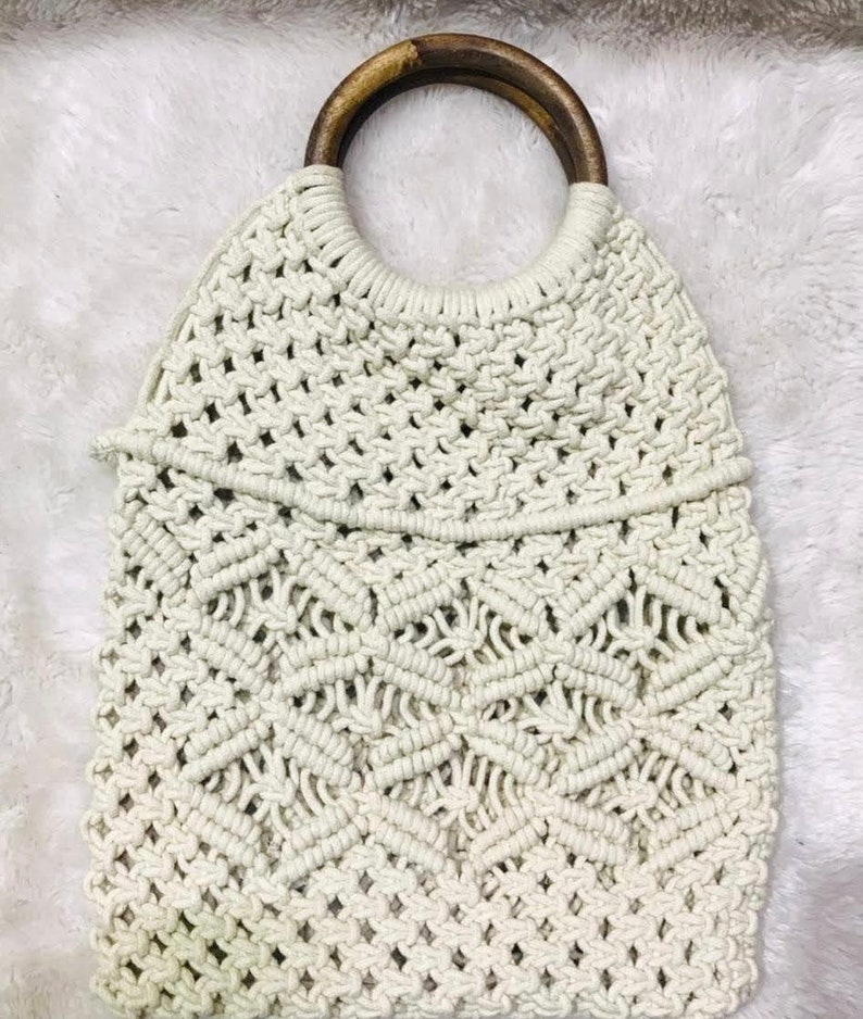 May include: A white crocheted tote bag with a wooden handle. The bag has a geometric pattern and is made of thick rope.